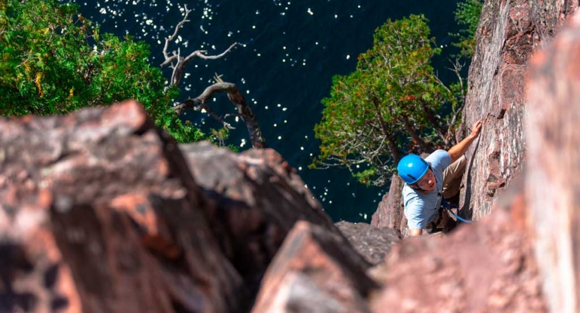 A person who is rock climbing is pictured below the camera. There is water below the climber. 